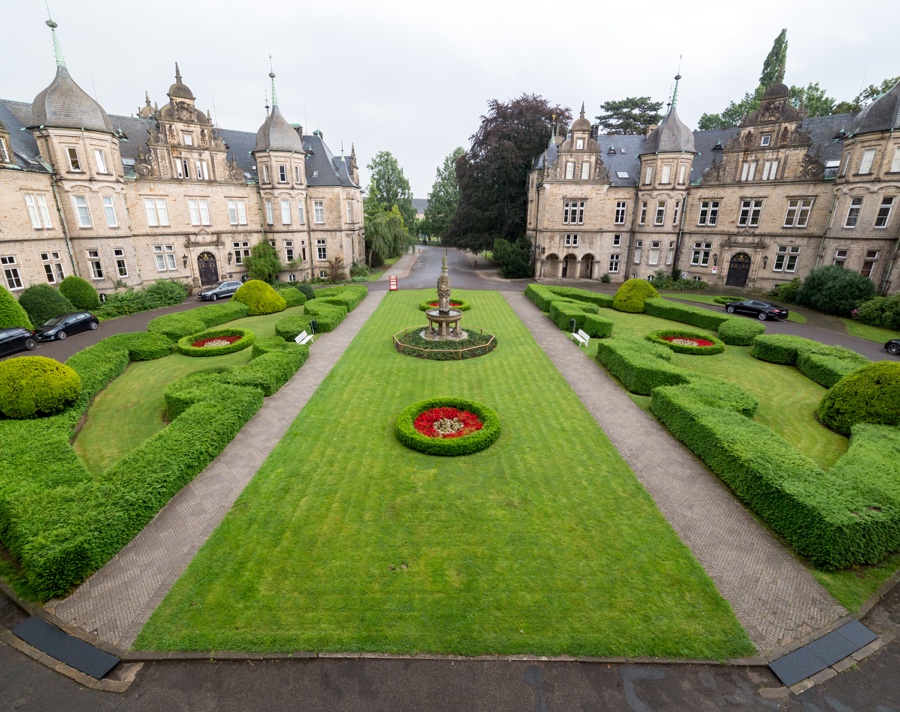 Schloss-Bückeburg-Vorgarten-900 - Reinweiss Hochzeiten Vorgarten des Schlosses Bückeburg mit gepflegten Rasenflächen, Blumenbeeten und einem zentralen Brunnen.
