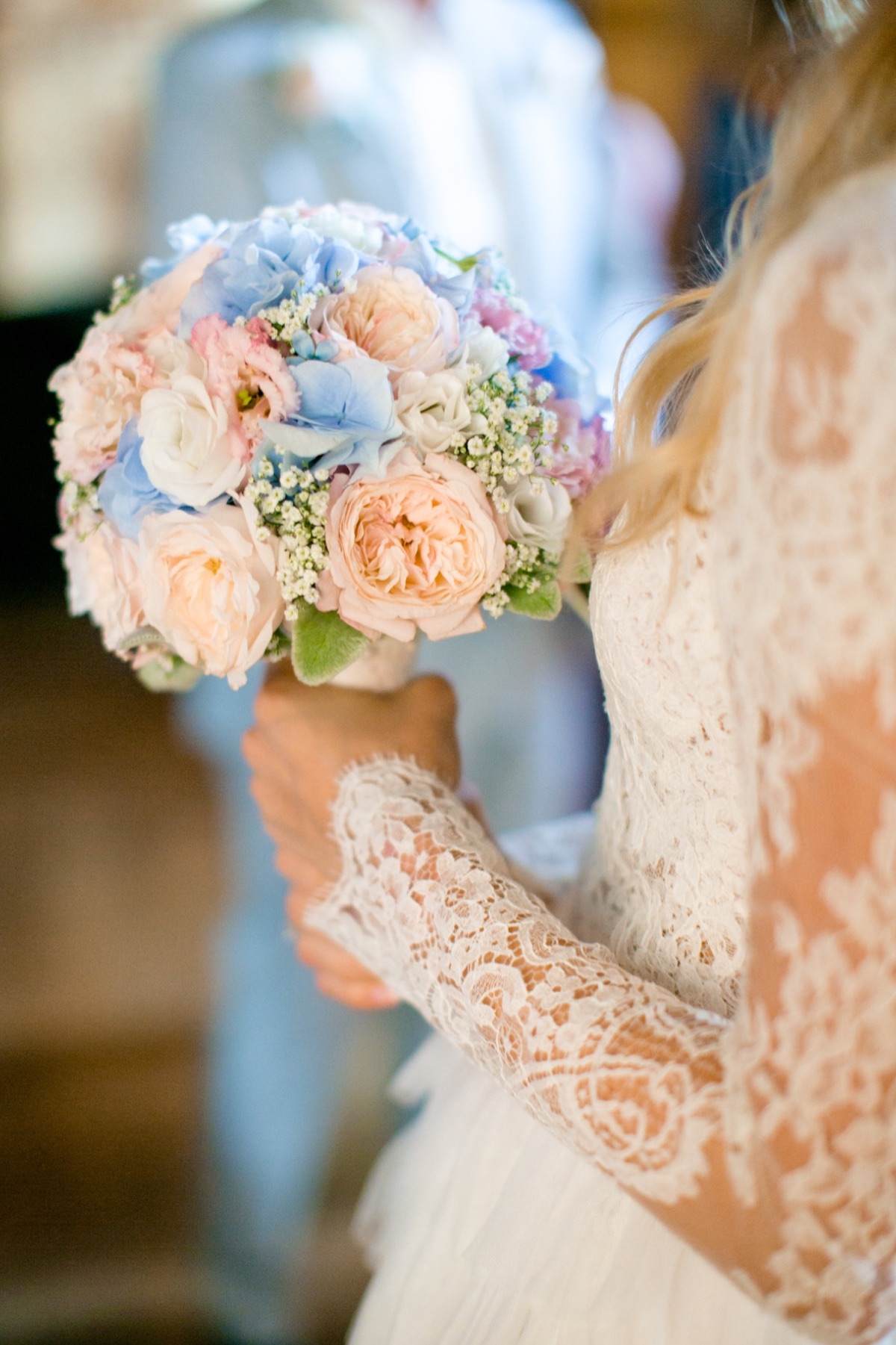 g-1 - Reinweiss Hochzeiten Braut hält einen bunten Blumenstrauß mit rosa, blauen und weißen Blumen in einem festlichen Raum.