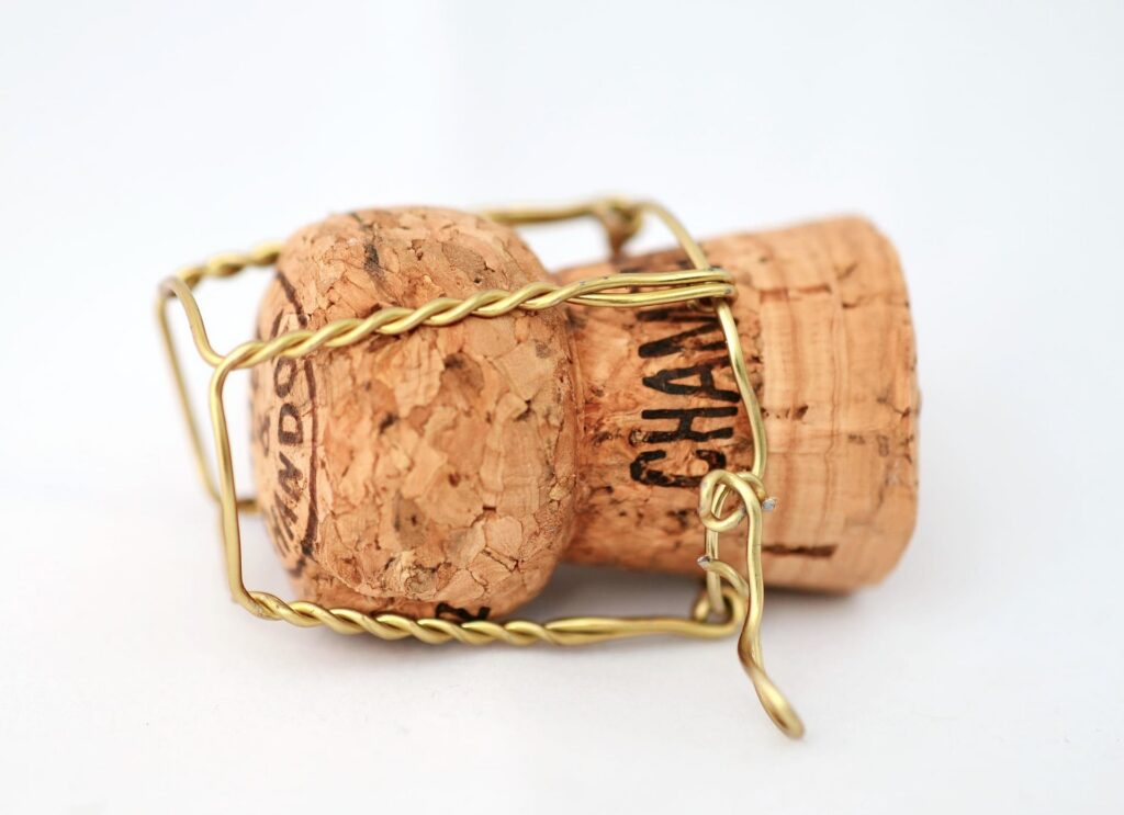 Quiet-luxury-wedding-champagne - Reinweiss Hochzeiten Korken einer Champagnerflasche mit Drahtkorb auf weißem Hintergrund, passend zum Thema einer eleganten Hochzeit.